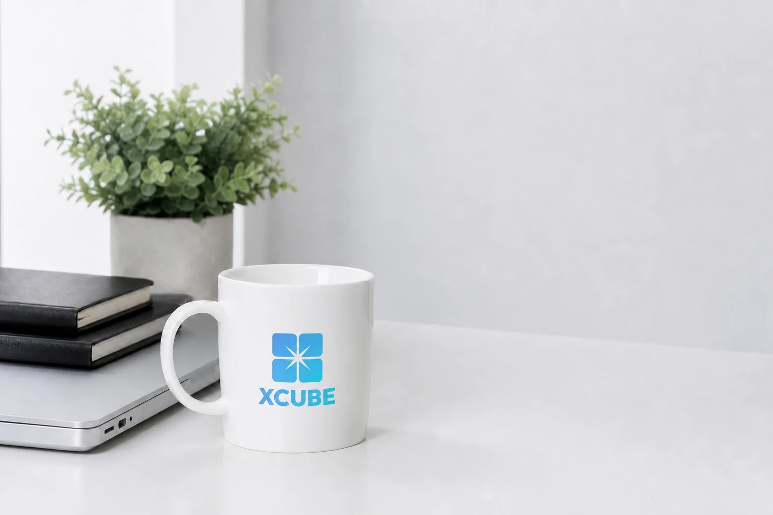 xCube branded cup beside a laptop and notebooks